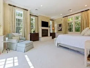 A bedroom with white bedding, a bench at the foot of the bed and tall shuttered windows.