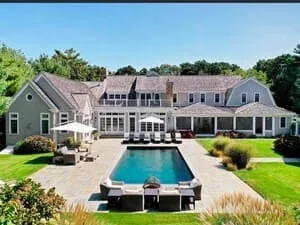 Aerial view of a shingled estate with a pool, pool house and clipped hedging.