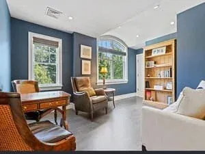 A study with blue walls, a built-in bookcase, a writing desk and upholstered armchairs.