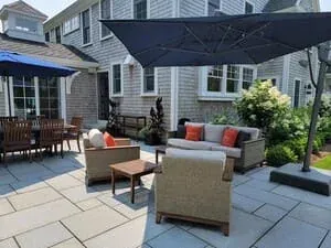 A stone patio with a retractable awning, outdoor sofas and a dining table beside the house.