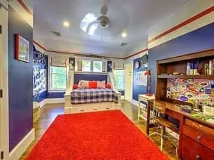 A child bedroom with blue walls, a red rug, a built-in bed and shelves of memorabilia.