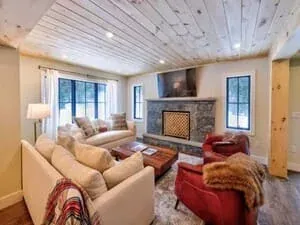 A living room with a stone fireplace, a planked ceiling, white sofas and a red throw.
