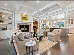 An open-plan living room with a brick fireplace, built-in shelving and a bank of windows.