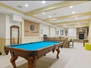 A finished basement games room with a pool table, a beamed ceiling and a dartboard on the wall.