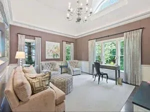 A living room with a chandelier, full-length curtains, a writing desk and neutral seating.