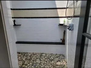 A dark-clad exterior wall with a pebble drainage bed and an outdoor shower fitting.