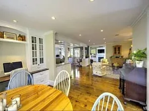 An open-plan living and dining room with white built-ins, a bay of windows and a wooden dining table.