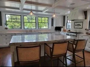 A kitchen with a large island and bar stools, a coffered ceiling and wide-plank floors.