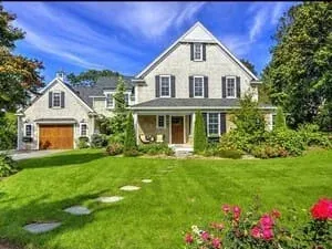A shingled house with white trim, an attached garage and a stone path across a green lawn.