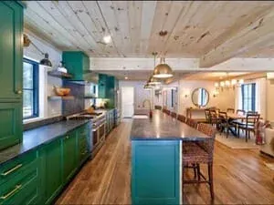 A kitchen with deep green cabinetry, a planked ceiling, a teal island and pendant lighting.