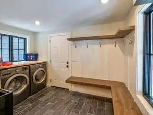 A mudroom and laundry with a front-loading washer and dryer, a wood shelf and hooks.