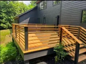 A deck with horizontal timber railings against dark siding, planting below.
