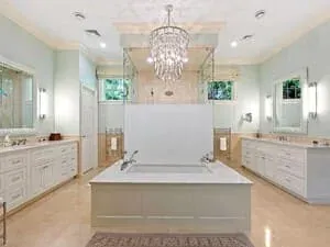 A bathroom with a chandelier over a freestanding tub, twin vanities and a soft green scheme.