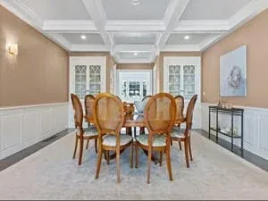 A dining room with wainscoting, cane-backed chairs and a round table on a pale rug.