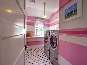 A laundry room with pink and white striped walls, a washer and dryer and a spotted floor.