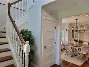 A white staircase with a turned newel post and a panelled wall in a bright hallway.