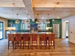 A kitchen with teal cabinetry, exposed beams, a long island and a row of wooden bar stools.