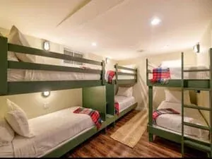 A bunk room with built-in bunks, green bedding and reading lights set into the panelling.