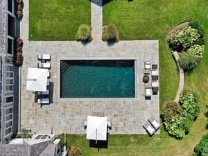Aerial view of a pool with loungers, a stone surround and planting beds around the lawn.
