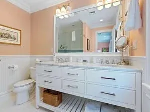 A bathroom with a white vanity, a framed mirror and soft pink walls.