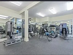 A home gym in a finished basement with weight machines, free weights and a mirrored wall.