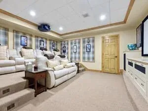 A basement lounge with a sectional sofa, a wall-mounted television and recessed lighting.