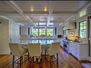 A kitchen with a marble island, bar stools and a bank of windows over the sink.