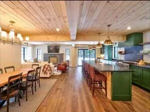 A kitchen and dining area with a green island, a planked ceiling and a hanging light over the table.