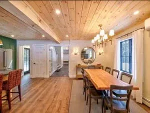 A dining room with a planked ceiling, a chandelier over a long table and a round mirror.